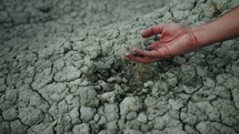 Farmer's hand touches dry soil