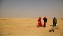 women covered in scarves walking through the desert 