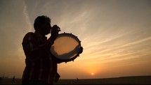 man playing a tambourine at sunset 