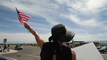 A woman waving an American flag on a street corner