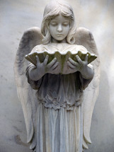 An Angelic female character statue holding an oyster shell in a historic cemetery in the southeastern United States as a grave marker and symbol of eternal rest among the Heavenly host of angels and God. 