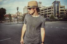a man in a hat standing in a parking lot in a city 