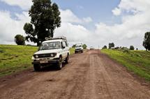 White sports utility vehicles travel down a remote dirt road.