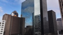 Pan out from a downtown Houston, Texas, building to show a glass-mirror skyscraper with a beautiful blue sky, clouds, and other miscellaneous buildings.