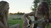 friends sitting on a blanket in the grass playing the guitar and singing 