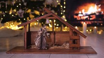 Woman placing Jesus Christ Nativity figurines near Christmas tree in front of fireplace. Christmas scene. 