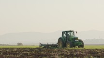 Tractor cultivating a green field in slow motion.