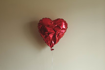 red heart shaped balloon against a beige wall