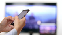 Woman hands texting on smartphone in front of tv close up.