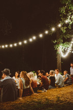 Guests sitting at an outdoor table lit by strings of lights.