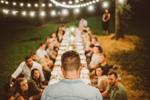 friends sitting on the ground for an outdoor dinner party praying 