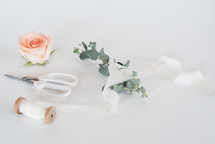 scissors, spool of ribbon, and flowers on white background 