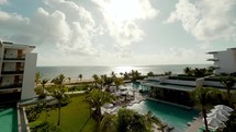 Cancun, Mexico beach resort timelapse with beautiful blue skies with clouds, palm trees, pools, and a view of the ocean.