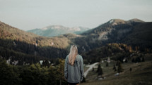 a woman standing with her back to the camera looking out at mountains 