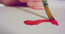 Macro shot of someone painting on paper with red acrylic paint.