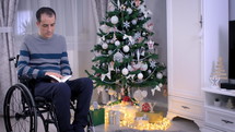 Christian man in wheelchair reading the Bible in front of Christmas tree. Spiritual time and studying the Bible concept. Dolly shot 