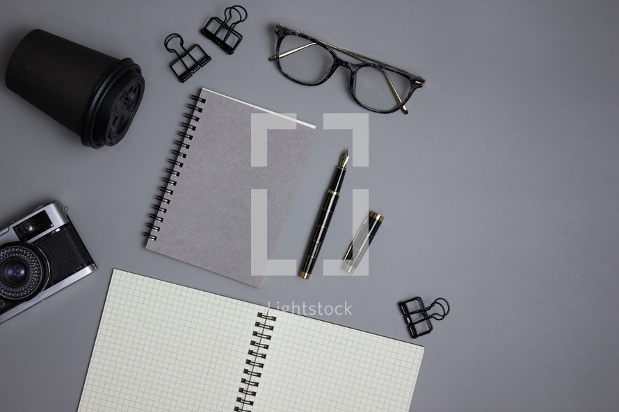 Glasses, cup, camera, notebook and office supplies on gray background