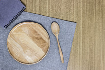 wooden plate, spoon, placemat, and notebook on a table 