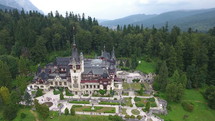 Aerial shot of Peles Castle in forest, Transylvania, Romania. Tourists visit the Peles castle, a masterpiece of Neo-Renaissance style, built between 1873 and 1914, the first European castle entirely lit by electrical current.