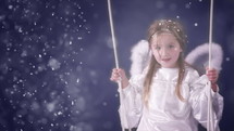 Young girl dressed as an angel, swinging, and smiling while it is snowing.