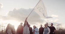 Wide shot of a small group waving a flag of Victory at sunset.