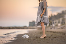 a girl in a dress standing on a beach next to a seashell 