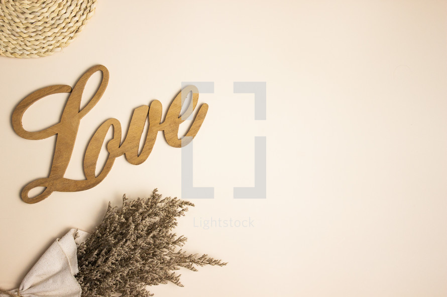 Wooden word love with dried flowers on tan background