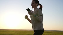 Fitness athlete in sportswear during outdoor running session. A young woman runner is listening to music in earphones and training in summer. Concept of workouts running and healthy lifestyle.