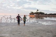 a couple holding hands running on a beach 