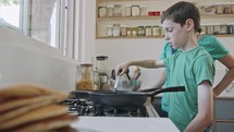 Boy preparing pancakes with his mother for breakfast in the kitchen