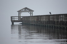 Bird sitting on a pier on the water at dusk.