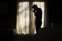 silhouette of a man with praying hands standing in front of a window 