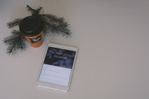 Bible app on an iPad, coffee cup, and pine boughs