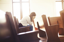a woman hiding her face in her hands sitting in a church pew 
