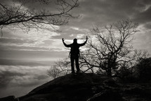 silhouette of a man standing on a mountaintop with raised hands 