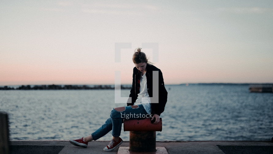  a woman sitting at a harbor at sunset 