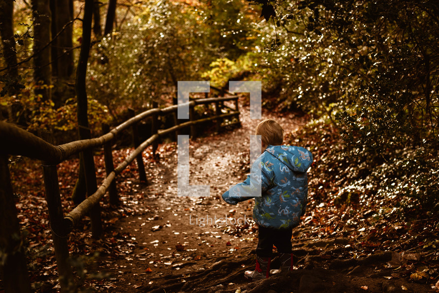 a toddler in boots walking on a trail in a fall forest 