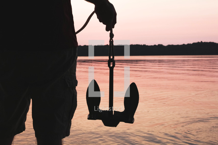a man holding an anchor at sunset