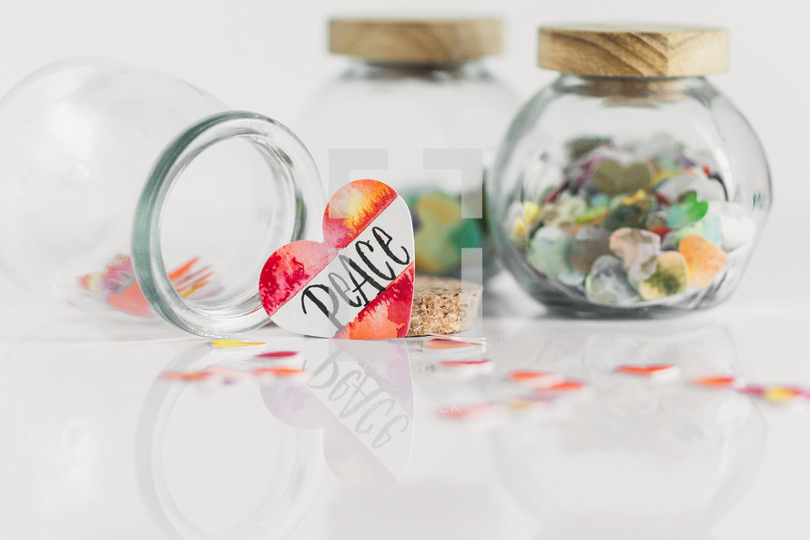 Jars of paper hearts on a white background with one lettered PEACE in front.