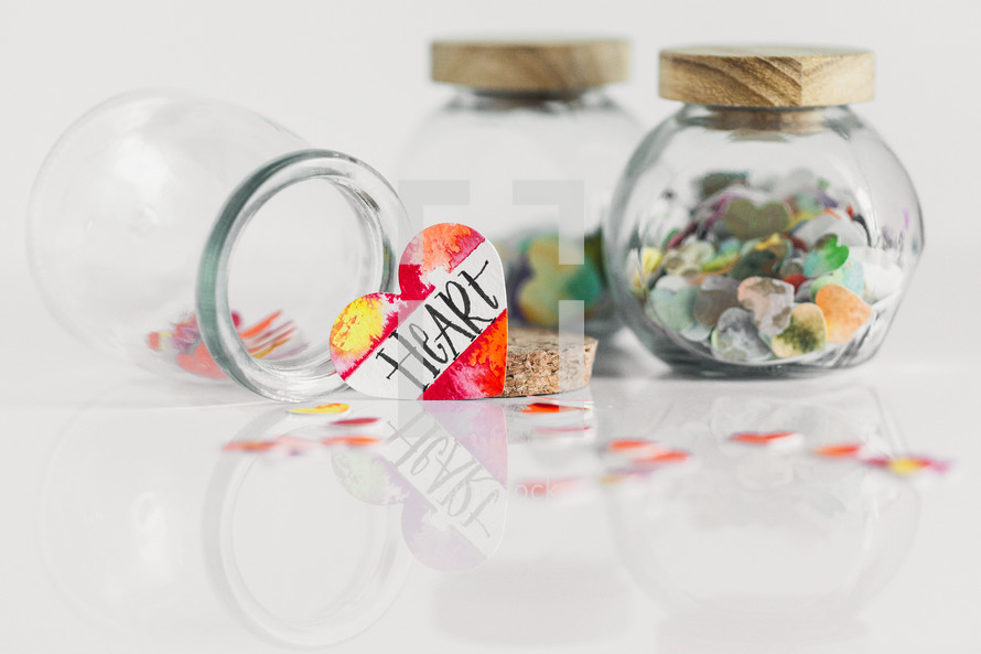 Jars of paper hearts on a white background with one lettered HEART in front.
