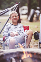 a little boy in pajamas sitting by a campfire 