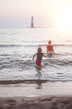 kids playing in the ocean at sunset in front of a lighthouse 