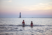 kids playing in the ocean in front of a lighthouse at sunset 