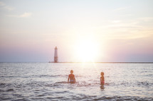 kids playing in the ocean with view of a lighthouse 