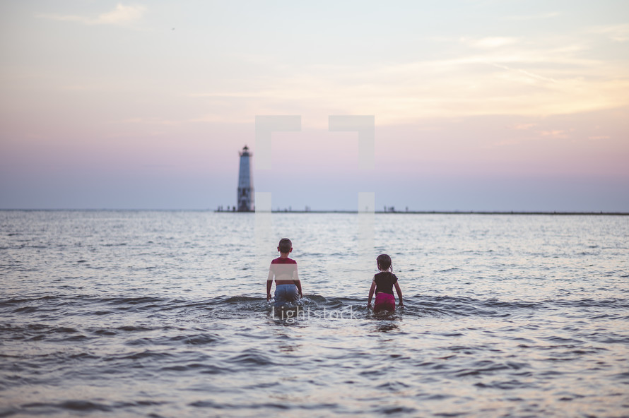 kids playing in the ocean in front of a lighthouse at sunset 