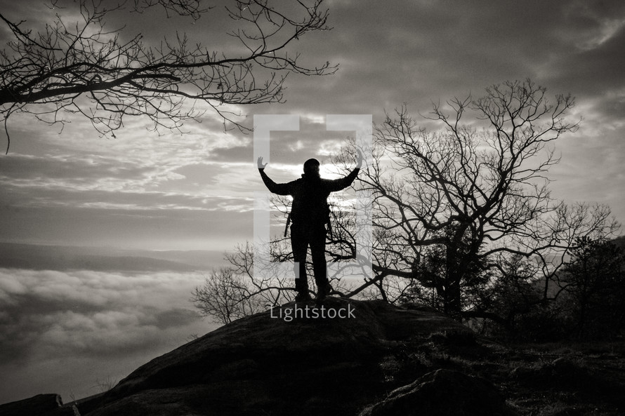 silhouette of a man standing on a mountaintop with raised hands 