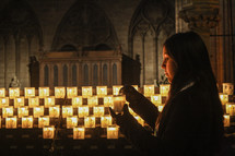 a woman lighting a prayer candle in a cathedral 