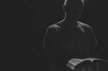 minister reading from a Bible under a spotlight