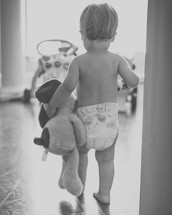 a toddler boy in a diaper carrying a stuffed animal 