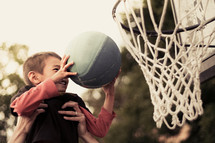 father lifting his son up to put a basketball in the net